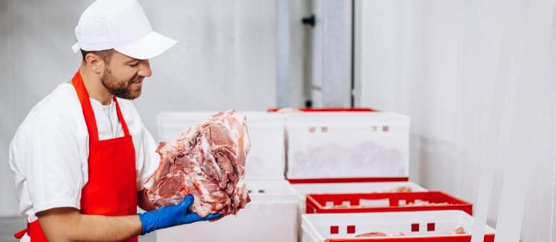 A worker of meat industry holds a big piece of fresh meat in his hands